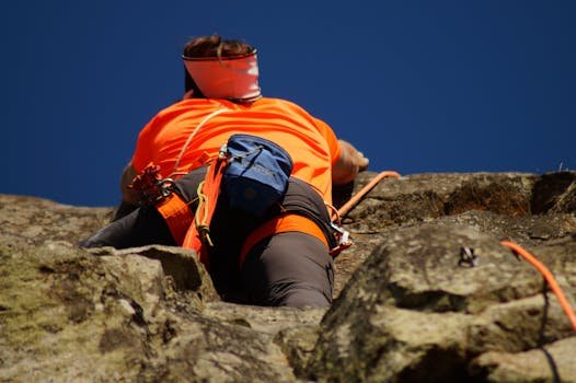 A climber in bright gear scales a rocky cliff, showcasing adventure and skill. Rock climbing harness