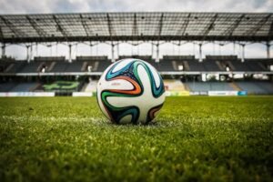 A vibrant soccer ball rests on a lush green field inside an empty stadium, capturing the essence of sports. for footballs page