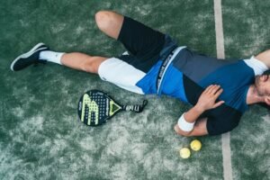 Tired young athlete resting on padel court with racket and balls nearby. for action sports equipment page