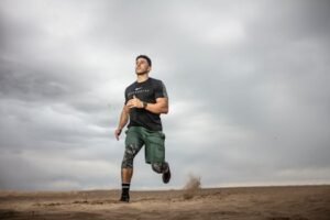 A muscular man running on sandy terrain under cloudy skies, promoting fitness and adventure. for action sports equipment page