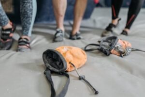 Close-up of climbing gear and chalk bags on gym mat with climbers in the background. climbing accessories