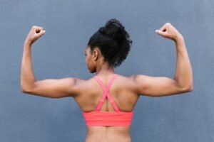 Rear view of a fit woman flexing muscles in a pink sports bra against a gray background. For fitness clothing page